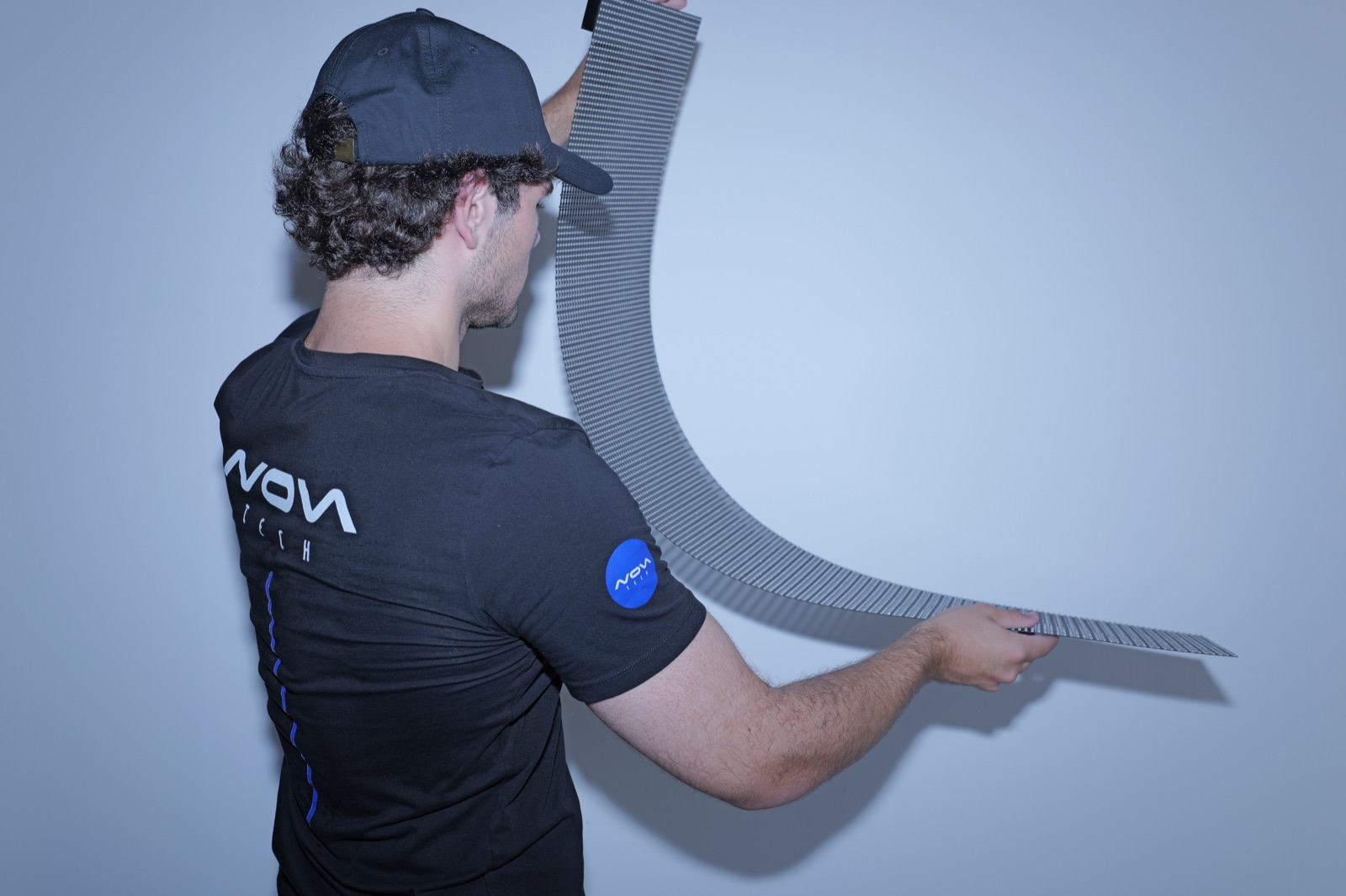 A NovaTech technician bending a flexible transparent LED mesh panel in the hand, showing how far it curves