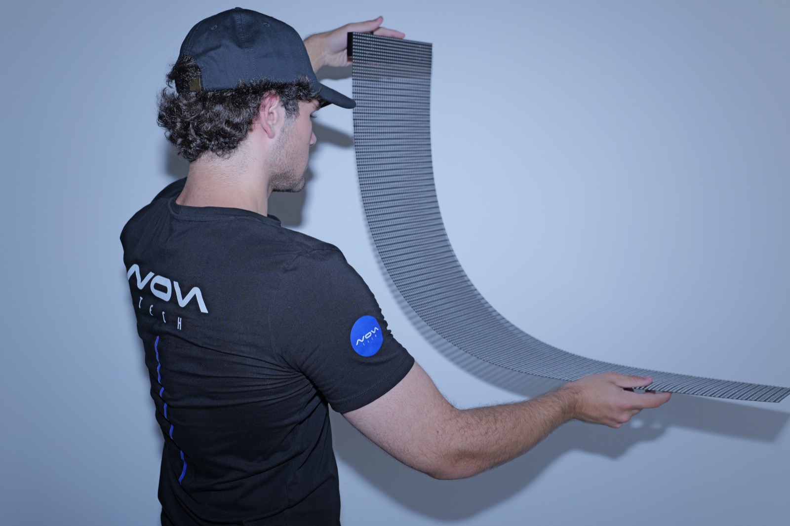 Flexible transparent LED mesh bending in a broad curve, city visible through the open lattice