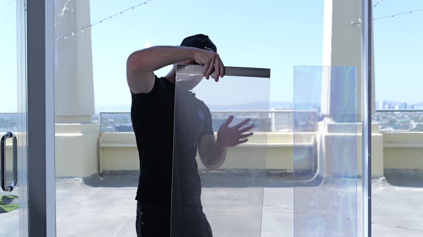 NovaTech Install specialist holding transparent LED film and mesh samples against floor-to-ceiling glass